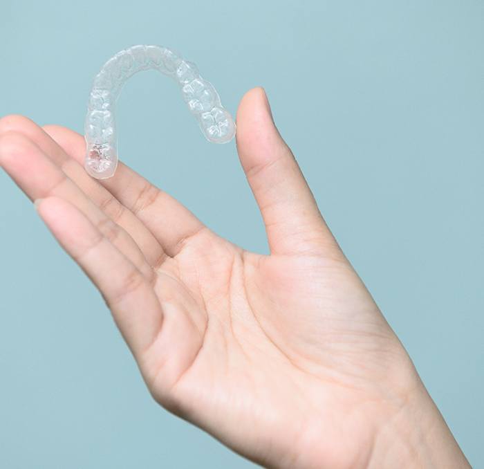 Patient holding clear aligner against blue background