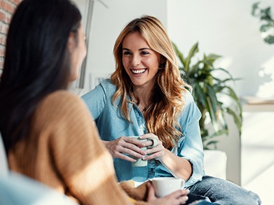 Woman smiling while drinking coffee with friend