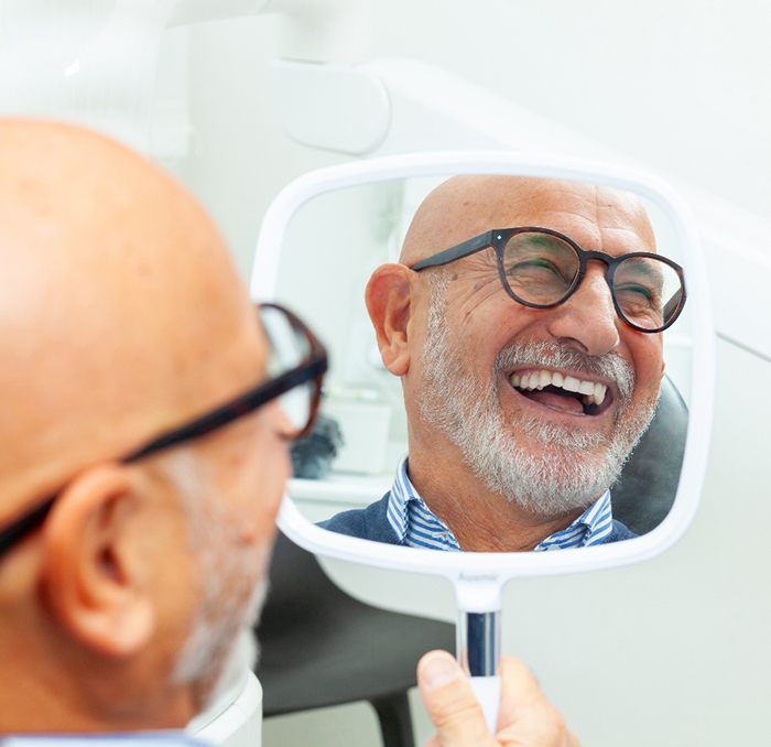 Man with glasses smiling at reflection in handheld mirror
