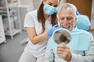 a man smiling in the mirror at the dentist’s office after receiving dental implants