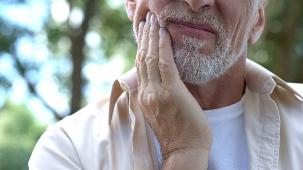 person experiencing dental emergency holding cheek during summer vacation